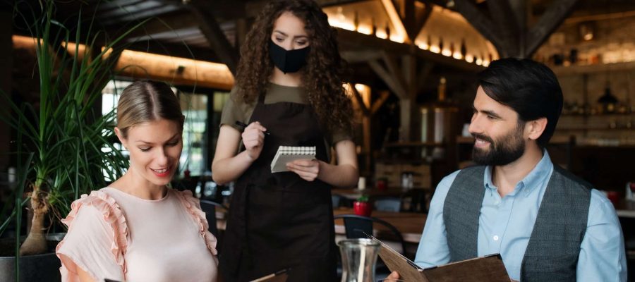 waitress-with-face-mask-serving-happy-couple-indoors-in-restaurant